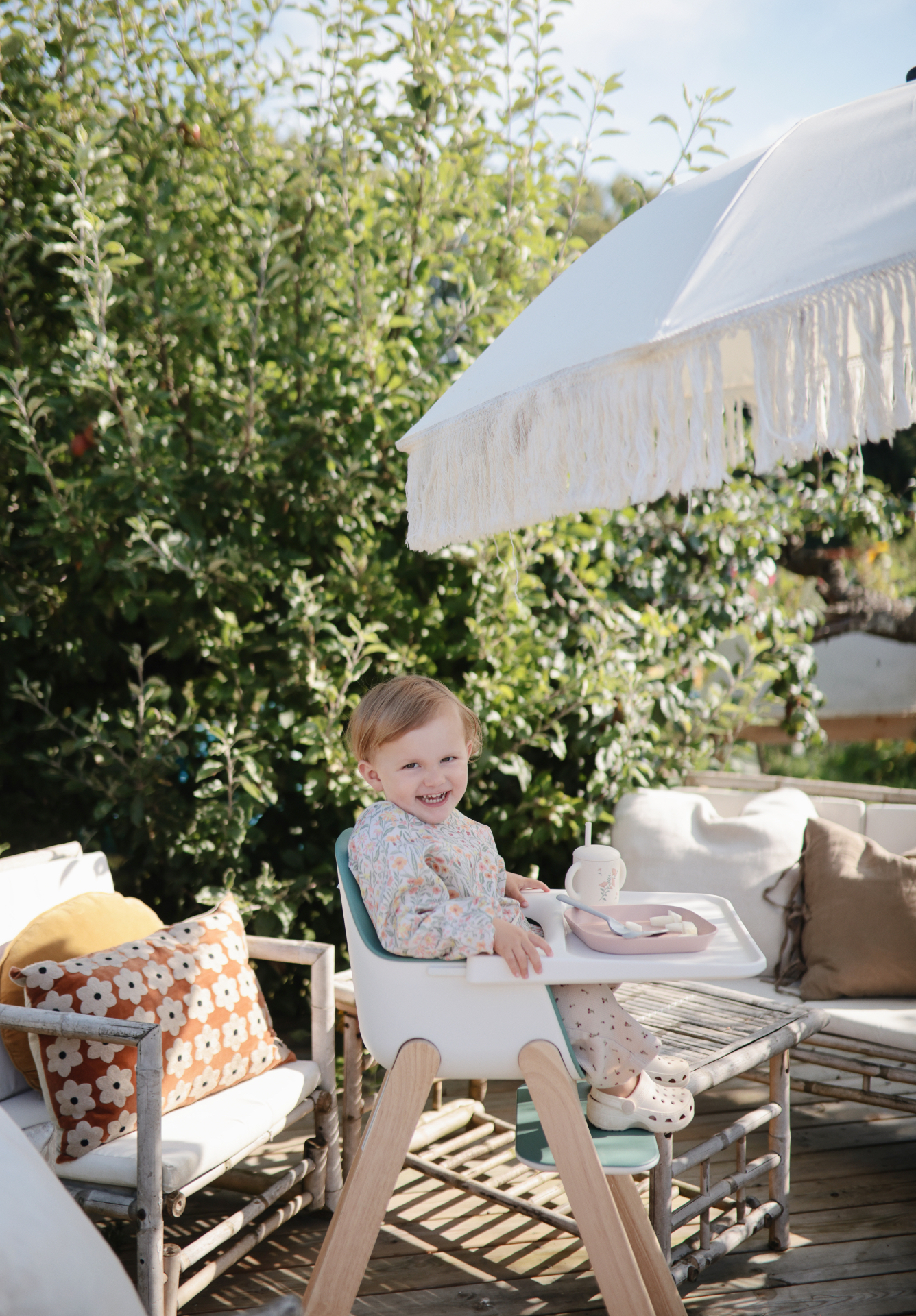 Toddler in a high chair with plate, cup and spoon outdoors